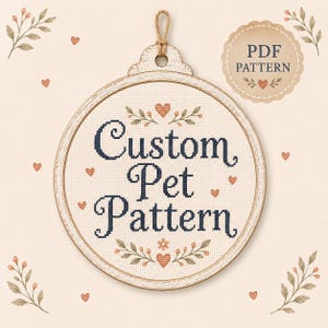 May include: A circular wooden embroidery hoop containing cross-stitch fabric with the dark blue text Custom Pet Pattern. The design features small orange hearts and green leafy sprigs. A beige scalloped badge in the corner reads PDF PATTERN.