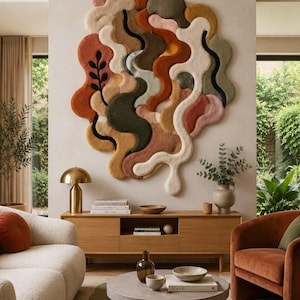 Op de afbeelding: Een groot, abstract wandkleed met organische, vloeiende vormen in een kleurenpalet van terracotta, saliegroen, mosterdgeel, crème en zwart. Het getextureerde, getufte oppervlak toont gebogen lijnen en een enkel zwart bladmotief.