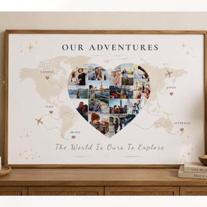 May include: A rectangular framed wall art print featuring a world map background with the text OUR ADVENTURES and The World Is Ours To Explore. A central heart-shaped collage displays various travel photographs, accented by small airplane icons.