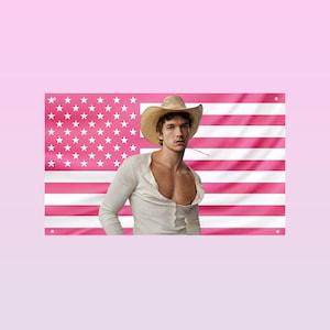 Op de afbeelding: Een rechthoekige wandvlag met een roze en wit horizontaal gestreept patroon en een roze veld in de linkerbovenhoek met witte sterren. Een persoon draagt een beige cowboyhoed en een wit shirt met lange mouwen en een knoopsluiting.