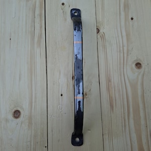 May include: A long, vertical metal door handle with a dark, weathered finish and two distinct copper-colored bands encircling the center. The handle features flat, rounded mounting ends at the top and bottom, each containing a single circular screw hole.