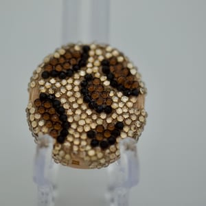 Puede incluir: Un anillo circular con un patrón de leopardo creado con pequeños cristales incrustados. El diseño consiste en piedras de color beige claro, marrón y negro dispuestas para imitar manchas de animal en toda la superficie del anillo.