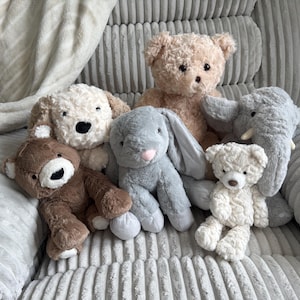 Könnte beinhalten: Eine Sammlung von sechs Plüschtieren, bestehend aus einem großen beigen Teddybären, einem cremefarbenen Hund, einem braunen Bären, einem grauen Hasen mit langen Ohren, einem kleinen cremefarbenen Teddybären und einem grauen Elefanten mit weißen Stoßzähnen.