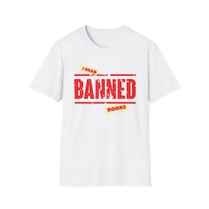 May include: A white short-sleeved t-shirt featuring a graphic design with the red text BANNED centred between two horizontal lines. Above and below the text are yellow rectangular accents with the words I READ and BOOKS printed in black.