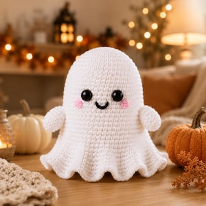 May include: A white crocheted ghost figure with a rounded head, small arms, and a flared base. The ghost features two large black plastic safety eyes, a stitched black mouth, and two small pink embroidered circles on the cheeks.