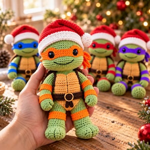 Può includere: Una bambola tartaruga all'uncinetto con pelle verde, guscio beige e maschera arancione, che indossa un cappello da Babbo Natale rosso e bianco. La bambola ha occhi a bottone neri e una cintura marrone con fibbia circolare. Tre bambole simili sono visibili sullo sfondo.