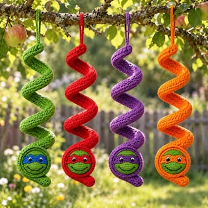 Puede incluir: Cuatro decoraciones colgantes de ganchillo en forma de espiral en verde, rojo, morado y naranja. Cada una tiene una base circular con una cara sonriente y un antifaz de color, que recuerda a una tortuga. Cuelgan de una rama mediante bucles.