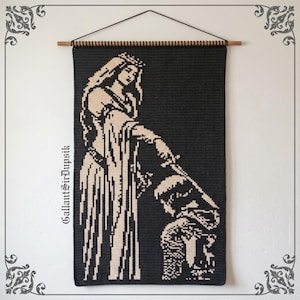 May include: A rectangular black and cream crochet wall hanging featuring a queen figure standing and holding a sword over a kneeling knight. The text GallantSirDupsik is printed vertically on the left side. It hangs from a wooden dowel.
