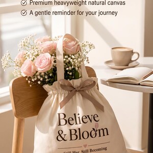 Peut inclure: Un sac fourre-tout en toile naturelle avec cordon de serrage portant le texte Believe & Bloom et Still Her. Still Becoming. Le sac est dot&eacute; d'un ruban marron et contient un bouquet de roses rose clair et de fleurs de gypsophile blanches.
