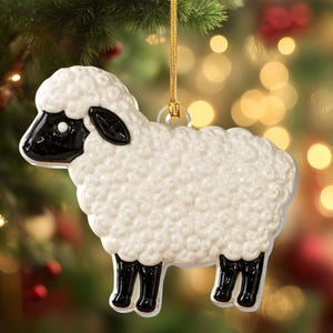 Peut inclure: Une décoration de Noël en forme de mouton avec un corps blanc texturé brillant représentant la laine, une tête noire lisse, des oreilles noires et quatre pattes noires. La décoration est suspendue par un cordon doré fin fixé à une boucle transparente.