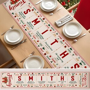 May include: A white fabric table runner featuring the red text "Family SMITHS" and various names like Richard, Sophia, and David. It includes green Christmas tree icons, red ornaments, and Bible verses such as "Trust in the Lord" and "He restores my soul" printed in a decorative, festive layout.