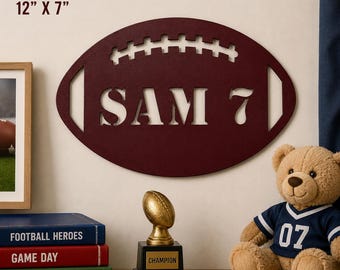 Pode incluir: Uma placa de parede oval de aço calibre 14 na cor bordô, em formato de bola de futebol americano com o texto recortado SAM 7. A placa mede 30,48 cm por 17,78 cm. Apresenta um design clássico de cadarços na parte superior e extremidades pontiagudas.