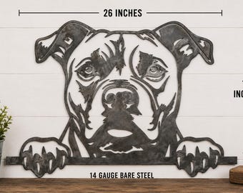 Pode incluir: Uma peça de arte de parede em metal cinzento-escuro com a forma de uma cabeça de cão com patas apoiadas numa barra horizontal. O design recortado é de aço nu de calibre 14 e mede 66,04 cm de largura por 40,64 cm de altura, conforme indicado.