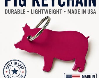 Pode incluir: Um porta-chaves em forma de porco cor-de-rosa brilhante com um anel de metal prateado. O texto PIG KEYCHAIN, DURABLE, LIGHTWEIGHT, MADE IN USA é visível. Um emblema circular diz BUILT TO LAST EVERYDAY USE com uma estrela, e um emblema retangular mostra a bandeira dos EUA e MADE IN USA.