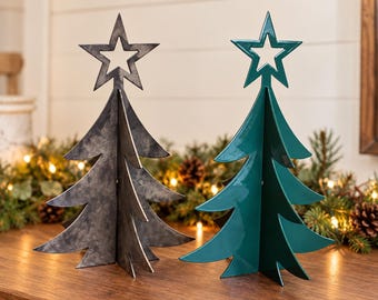 Pode incluir: Duas esculturas de árvore de Natal em metal independentes, uma com acabamento cinza escuro desgastado e a outra com acabamento verde escuro liso e brilhante. Cada árvore apresenta uma estrela recortada no topo.