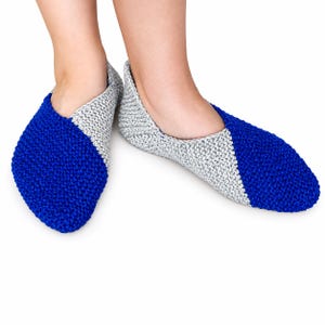 Op de afbeelding: Een paar handgebreide pantoffels met een kleurblokontwerp. Elke pantoffel is gemaakt met een diagonaal patroon van fel koningsblauw en lichtgrijs gemêleerd garen, met een textuur van ribbelsteek over het gehele zichtbare oppervlak.