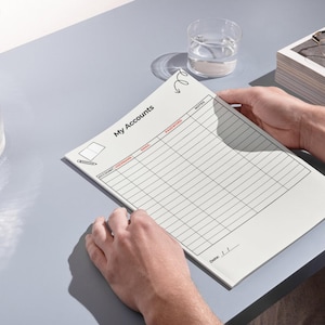 Könnte beinhalten: Ein weißes Blatt Papier mit der Überschrift My Accounts und einem Rasterlayout zur Erfassung von Kontoinformationen. Die Tabelle enthält Spalten für Account, Username, Email, Password und Notes. Ein kleines Symbol eines Notizbuchs ist zu sehen.