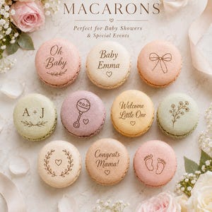 May include: A collection of round, pastel-colored macarons featuring custom engravings including text like Oh Baby, Baby Emma, A + J, Welcome Little One, Congrats Mama, and illustrations of a bow, rattle, flowers, and baby footprints.