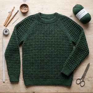 Peut inclure: Un pull à manches longues vert forêt foncé avec un motif en maille gaufrée texturée, un col rond, ainsi que des poignets et un ourlet côtelés. Le pull est présenté avec une pelote de laine assortie, deux crochets en bois, des marqueurs de mailles, des ciseaux et un ruban à mesurer.