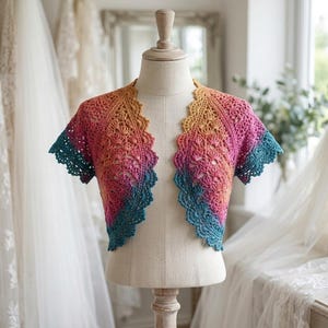 May include: A short-sleeved crochet bolero featuring a vibrant gradient color pattern that transitions from golden yellow at the neckline to magenta pink in the center and deep teal blue along the scalloped edges, displayed on a mannequin.