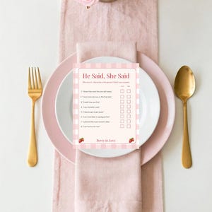 Op de afbeelding: Een rechthoekige spelkaart met de titel He Said, She Said, een lichtroze en witte gingham-rand en kleine aardbei-illustraties. De kaart bevat acht genummerde stellingen met selectievakjes en de tekst Berry in Love.