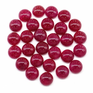 May include: A collection of twenty-five circular, smooth, and polished cabochons in a deep ruby red color. Each piece features a domed top surface with a reflective finish, arranged in a loose, circular cluster against a plain white background.