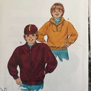 May include: Sewing pattern for two boys' jackets. The pattern is called "Kwik Sew" and is for sizes 4-5-6-7. One jacket is a maroon bomber jacket with a zipper closure. The other jacket is a yellow pullover with a mock neck and a zipper closure. The pattern is designed by Kerstin Martensson.