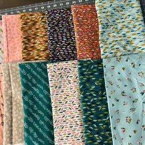 May include: An assortment of folded fabric pieces featuring diverse patterns and colours. Designs include leaf, floral, and arrow motifs in shades of pink, green, blue, and brown. The fabrics are arranged on a grey cutting mat.