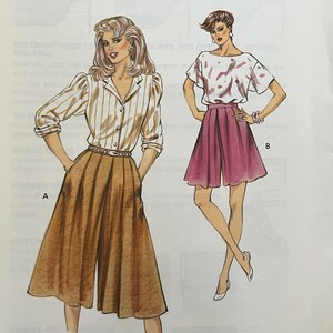 Puede incluir: Patrón de costura Kwik Sew 1424 con ilustraciones de dos conjuntos. Uno incluye una camisa a rayas con cuello y pantalones plisados. El otro incluye una blusa de manga corta y pantalones cortos plisados. Tallas 14-16-18-20.