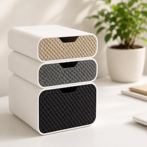 Peut inclure: Une pile de trois tiroirs de rangement rectangulaires avec des cadres extérieurs blancs. Chaque façade de tiroir présente une surface texturée à motif losange dans une couleur différente : beige en haut, gris foncé au milieu et noir en bas.