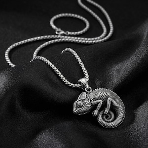 May include: A silver-toned metal necklace featuring a detailed chameleon pendant with a textured, scaled surface. The pendant hangs from a sturdy box chain, showcasing a curled tail and defined eye, crafted with an oxidised finish for depth.