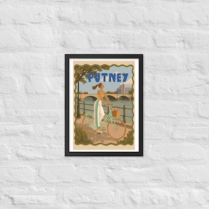 May include: A framed art print featuring a light green bicycle with a basket, a person in white pants and a tan top, and the text PUTNEY. The scene depicts a riverfront with a bridge, trees, and a building in the background, all enclosed in a wavy border.