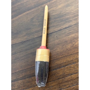 Può includere: Un pennello con manico in legno chiaro che riporta la scritta ADELE BISHOP in nero. Il pennello presenta una ghiera in metallo dorato, un piccolo anello rosso di accento e setole scure racchiuse in una guaina protettiva di plastica trasparente.
