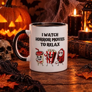 Puede incluir: Una taza de cerámica blanca con interior y asa negros, que presenta el texto negro I WATCH HORROR MOVIES TO RELAX y un gráfico de un vaso con cara de calavera, un cubo de palomitas y una figura con máscara de hockey y una motosierra.