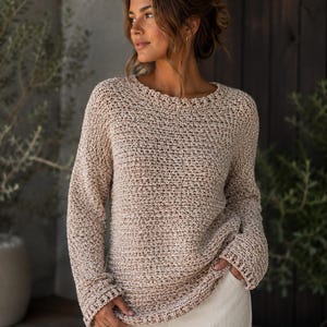Könnte beinhalten: Ein langärmeliger Pullover mit Rundhalsausschnitt und einem strukturierten Strickmuster aus hellbeigem und lohfarbenem meliertem Garn. Das Kleidungsstück hat eine lockere Passform mit leicht überschnittenen Schultern sowie gerippte Details an Ausschnitt, Ärmelbündchen und Saum.