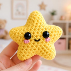 Puede incluir: Un peluche de ganchillo con forma de estrella amarilla y superficie de hilo texturizado. La estrella presenta dos ojos de seguridad negros, grandes, redondos y brillantes, una pequeña boca negra bordada y dos círculos rosas en las mejillas.
