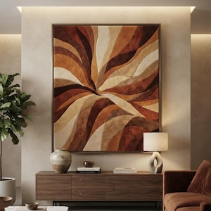 May include: A large square wall art piece featuring a textured, tufted design with swirling, organic waves in shades of cream, tan, rust, and dark brown. The artwork is encased in a thin, dark-toned frame and mounted on a neutral-coloured wall.