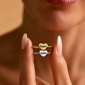 Peut inclure: Deux bagues superposées avec un design de bande torsadée. La bague supérieure est dorée avec une breloque en forme de cœur gravée du nom Rachel. La bague inférieure est argentée avec une breloque en forme de cœur gravée du nom Sophia.
