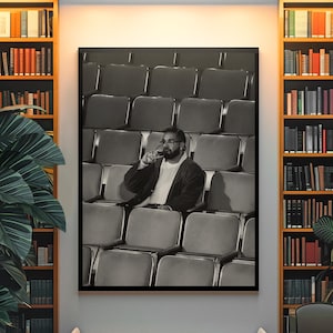 May include: A framed black and white wall art print depicting a person with a beard sitting alone in a large, empty theatre auditorium, holding a glass to their lips while wearing a dark jacket over a light-coloured shirt, centred on a wall.