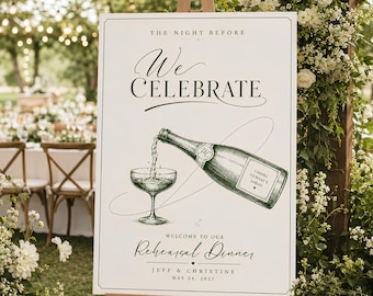 May include: A white rectangular sign with dark green text and a detailed illustration of a champagne bottle pouring into a coupe glass. The text reads: THE NIGHT BEFORE WE CELEBRATE, WELCOME TO OUR REHEARSAL DINNER, JEFF & CHRISTINE, MAY 24, 2027.