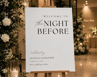May include: A white rectangular wedding welcome sign on a wooden easel featuring black text that reads: WELCOME TO the NIGHT BEFORE, Celebrating OLIVIA & ALEXANDER, AUGUST 21, 2027, We're so glad you're here. The sign has a clean, minimalist design.