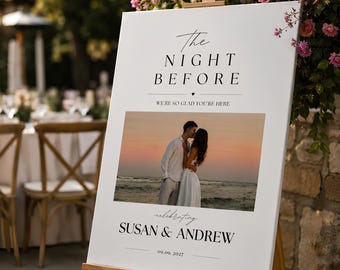May include: A white rectangular wedding welcome sign on a wooden easel featuring the text The Night Before, We're So Glad You're Here, Susan & Andrew, and the date 09.09.2027, with a central color photograph of a couple embracing on a beach at sunset.