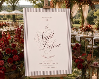 May include: A rectangular wedding welcome sign on a wooden easel featuring a white background with a dark red striped border. The text reads: WELCOME TO the Night Before let's celebrate ASHLEY AND JAMES 09.09.27 | PARIS, FRANCE in dark red.