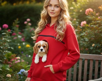 May include: A bright red hooded sweatshirt featuring a large front pouch with a zippered opening, designed to carry a small dog. The hoodie has long sleeves, ribbed cuffs, and a kangaroo pocket below the pet carrier section for storage.
