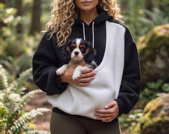 Puede incluir: Una sudadera con capucha en blanco y negro que cuenta con un gran bolsillo frontal diseñado para llevar a un perro pequeño. La sudadera tiene mangas largas, capucha con cordón y un cuerpo negro sólido con un panel blanco en contraste.