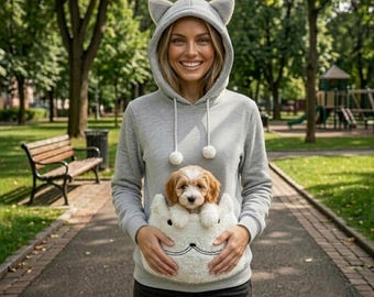 Puede incluir: Una sudadera gris claro de manga larga con capucha con orejas de gato y dos cordones con pompones blancos. La parte delantera incluye un bolsillo grande de felpa blanca para llevar un cachorro, con rasgos faciales de gato bordados en negro.