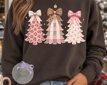 May include: A dark charcoal gray sweatshirt featuring a graphic of three stylized Christmas trees. The left tree is pink with leopard print, the center tree has a green and pink checkered pattern, and the right tree is white with pink polka dots.