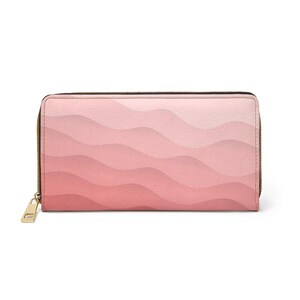 Op de afbeelding: Een rechthoekige portemonnee met ritssluiting en een getextureerd oppervlak met een roze ombre golfpatroon dat verloopt van licht pastelroze aan de bovenkant naar een diepere, verzadigde roze kleur aan de onderkant, met een goudkleurige metalen rits.