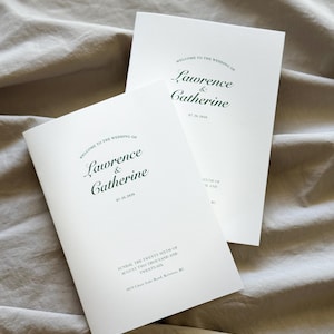 May include: Two white wedding programmes with dark green text. The text reads: Welcome to the wedding of Lawrence & Catherine, 07.26.2026, Sunday, the twenty sixth of August two thousand and twenty-six, 4870 Chute Lake Road, Kelowna, BC.