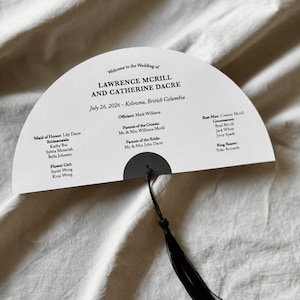 Puede incluir: Un abanico de programa de boda blanco en forma de semicírculo con texto negro que detalla la ceremonia de Lawrence Mcrill y Catherine Dacre el 26 de julio de 2026 en Kelowna, Columbia Británica, con un acento circular y una borla negros.